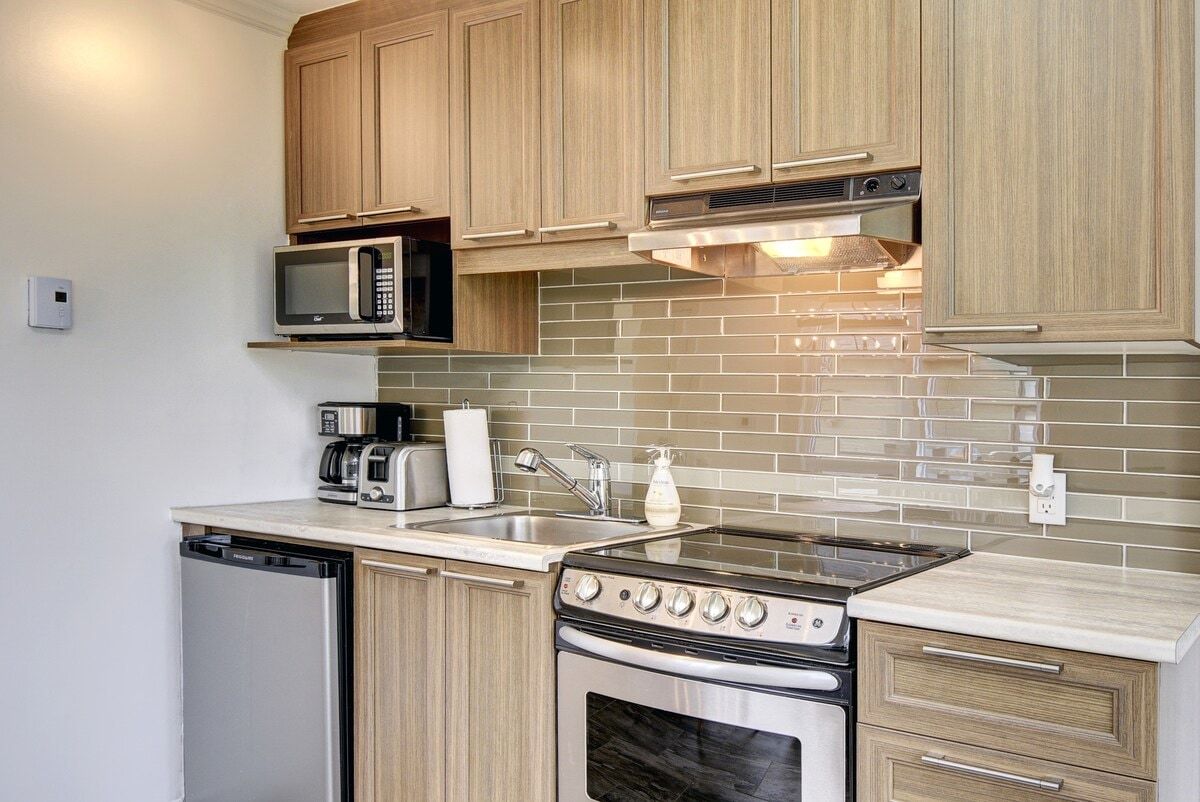 A compact kitchen with a dishwasher, microwave, stove, and a tiled backsplash.