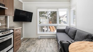 A modern kitchen with a built-in oven, a flat-screen TV, and a large window with a view of a residential area.