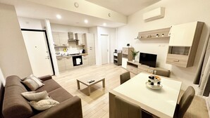 Ein modernes Wohnzimmer mit einem braunen Sofa, einem Esstisch mit Stühlen, einer Küchenzeile mit Herd und einem Fernseher.