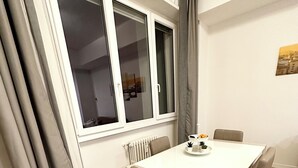 Ein Essbereich mit einem weißen Tisch, vier Stühlen, einem Fenster mit Vorhängen und einer Heizung.