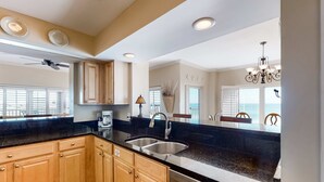 A kitchen with wooden cabinets, a black countertop, a double sink, and a ceiling fan.