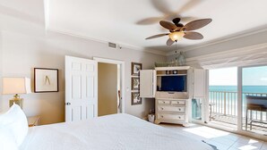 A bedroom with a bed, a ceiling fan, a TV, a dresser, and a balcony with a view.