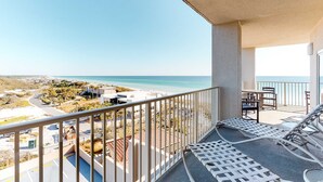 A balcony with a view of the beach and ocean, outdoor seating, and a pool area.