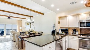 A kitchen with white cabinets, a granite countertop, stainless steel appliances, and a dining area with a table and chairs. - 2BR Gulf-front condo w/ private balconies (Miramar Beach)