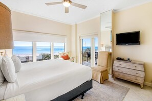 Ein Schlafzimmer mit einem großen Bett, einem Deckenventilator, einem Fernseher, einem Schminktisch und einem Balkon mit Meerblick.