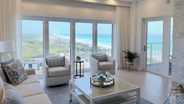 Ein geräumiges Wohnzimmer mit großem Fenster zum Strand, einem Glastisch und einem Balkon mit Aussicht.