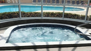 Un bain à remous avec vue sur une piscine et une plage, grâce à de grandes fenêtres.
