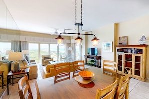A spacious living room with a dining area, a television, and a bookshelf. - 2BR Gulf View Condo: Steps to Beach & Pool (Miramar Beach)
