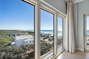 A room with large windows offering a view of a coastal area, a door with a curtain, and a tiled floor. - Gulf views from private balconies, beach access (Miramar Beach)