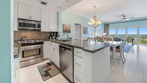 A modern kitchen with stainless steel appliances, a central island, and a dining area with a view. - Exclusive 3BR Beachfront with Gulf Views (Miramar Beach)