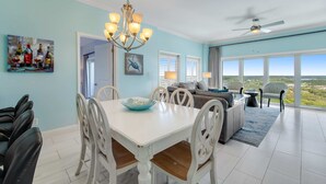 A spacious living area with a dining table, chairs, and a sofa. There is a ceiling fan, a large window with a view, and a chandelier. - Exclusive 3BR Beachfront with Gulf Views (Miramar Beach)