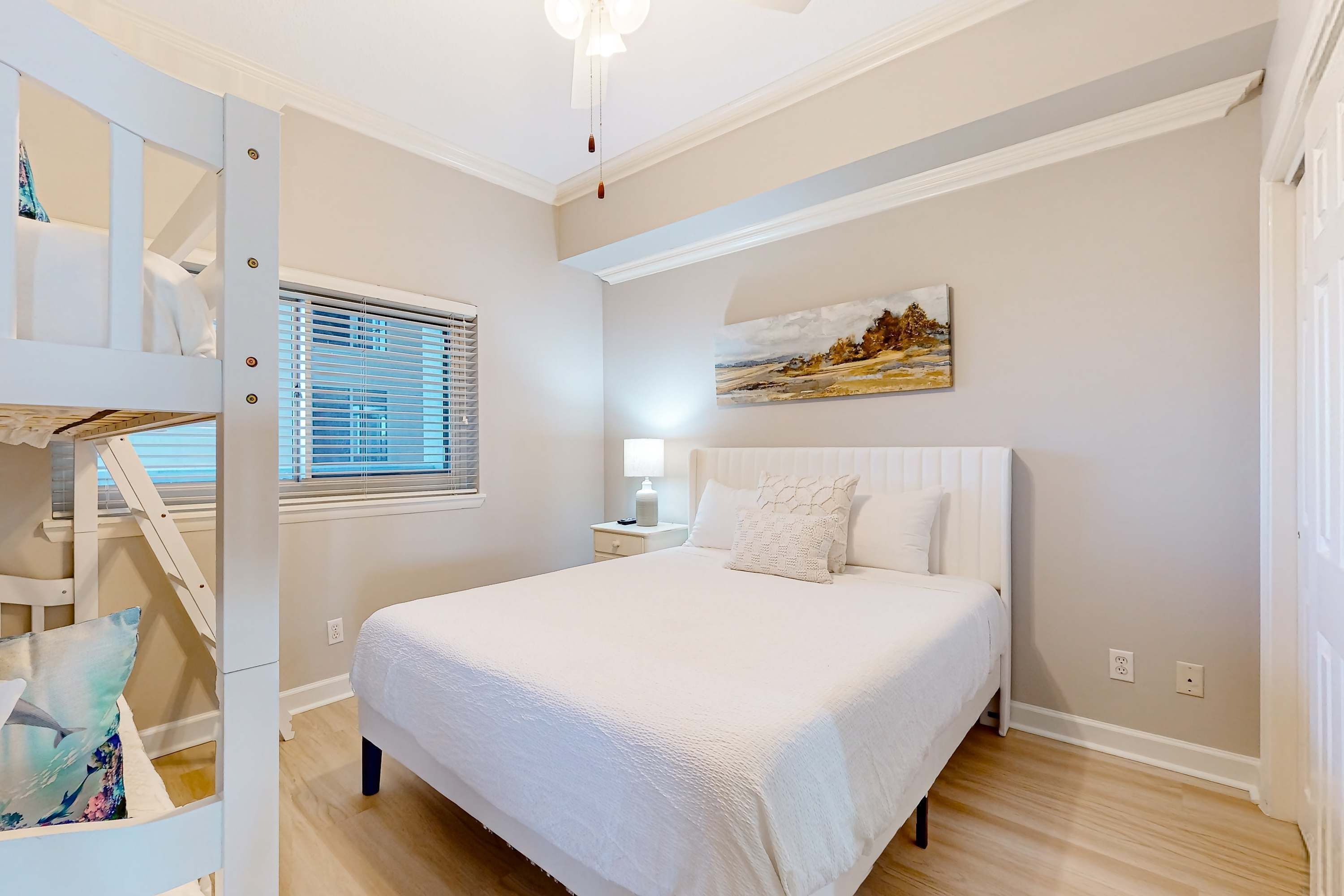 A bedroom with a bunk bed, a large bed, a painting on the wall, and a window with blinds.