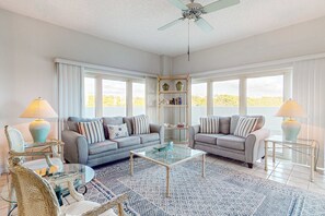 A living room with two sofas, a coffee table, a bookshelf, and a ceiling fan. - Beachfront luxury with panoramic Gulf views (Miramar Beach)