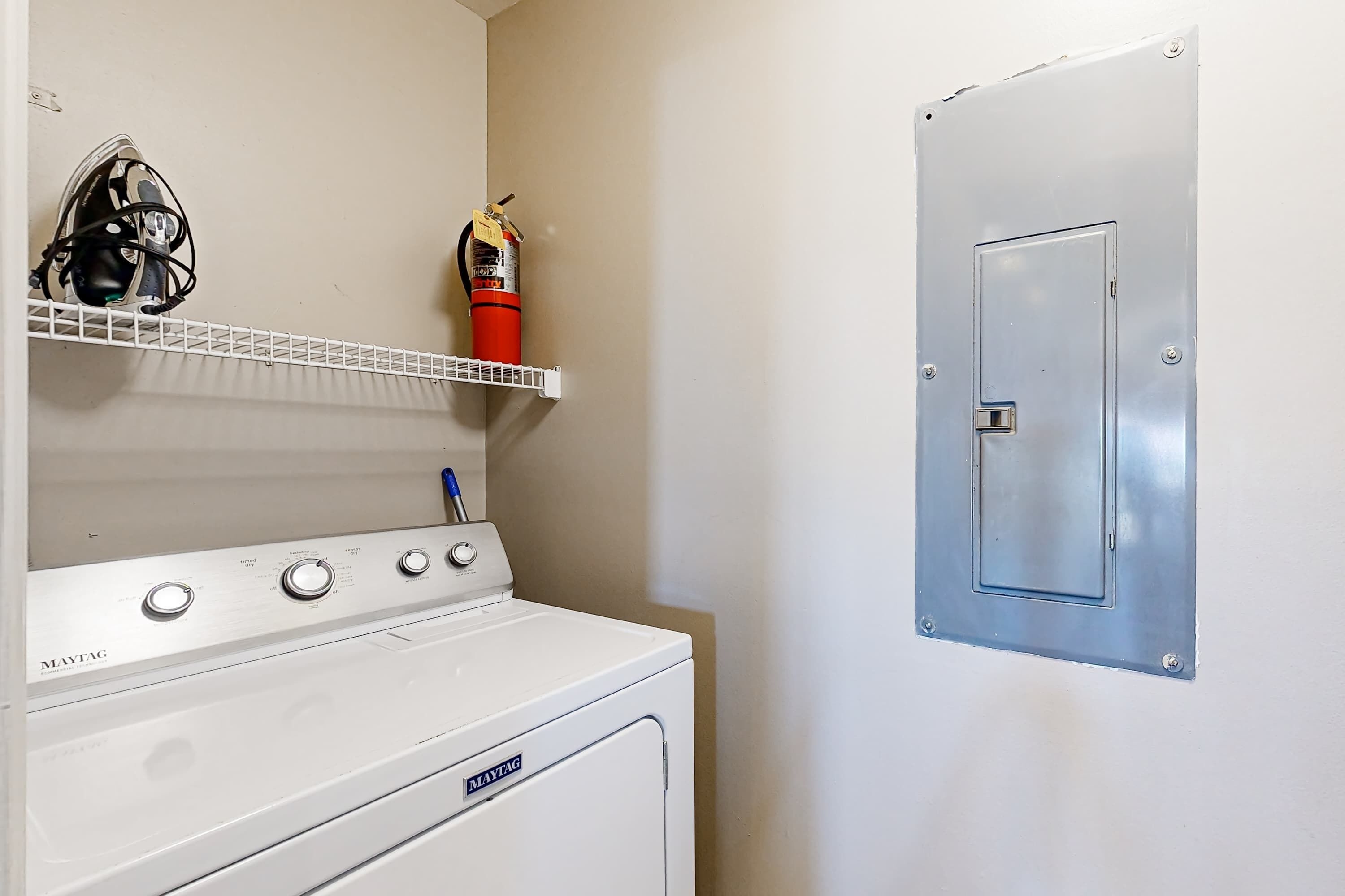 A laundry area with a Maytag washer and dryer, a fire extinguisher, and a metal door.