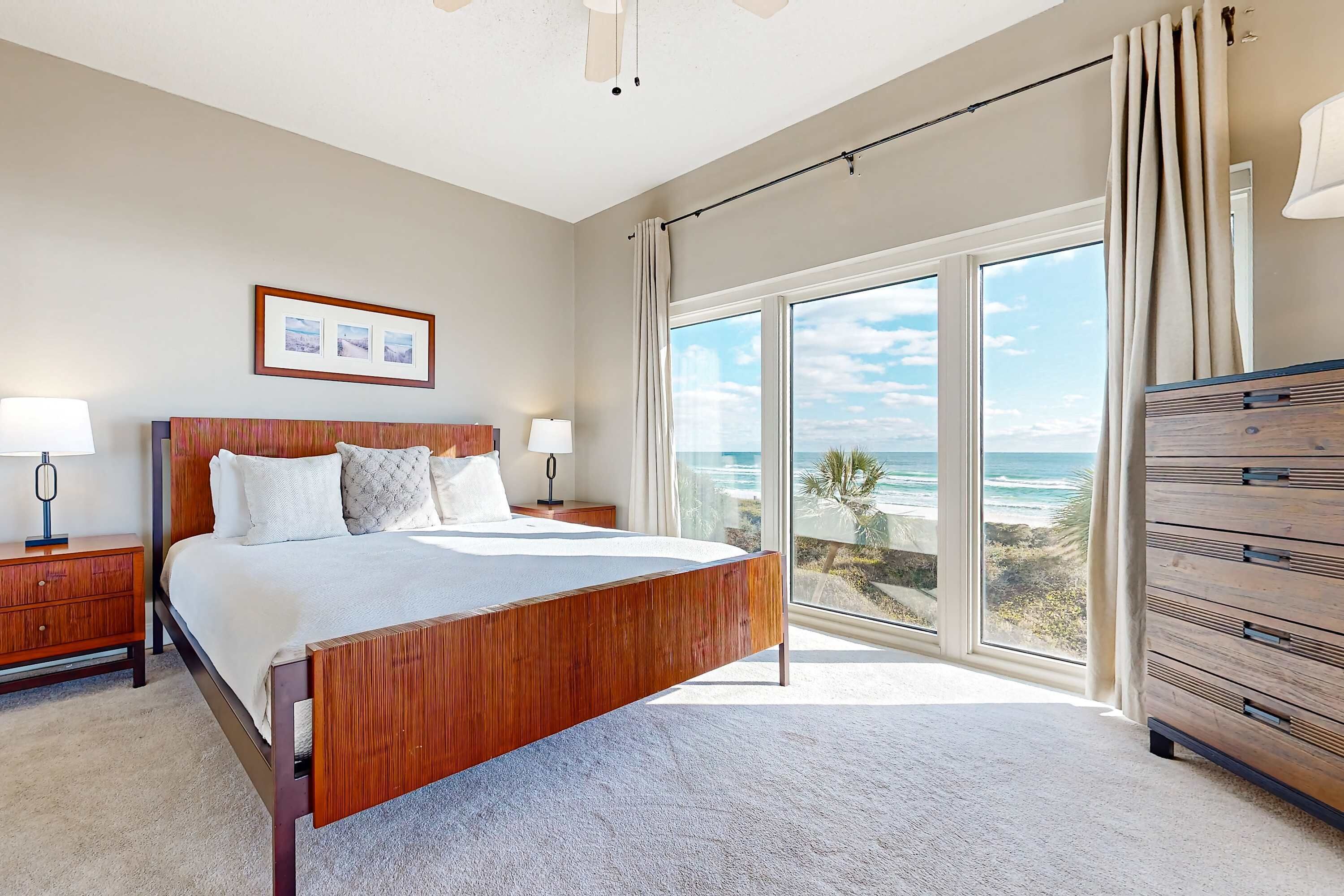 A bedroom with a large bed, a nightstand, a dresser, and a view of the ocean.