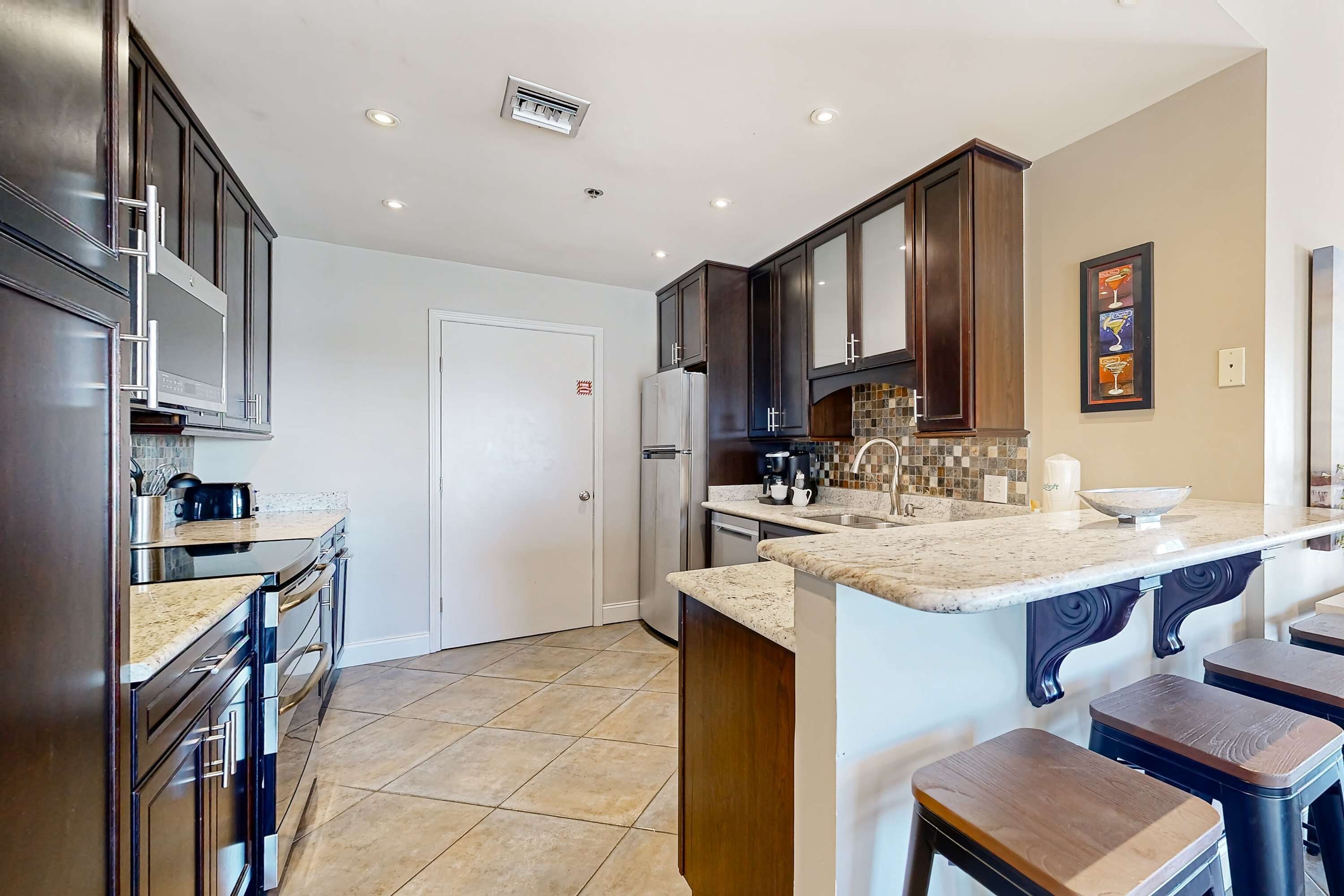 A modern kitchen with dark wooden cabinets, stainless steel appliances, and a marble countertop.
