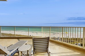 Ein Balkon mit zwei Lounge-Stühlen und einem Tisch, mit Blick auf einen Strand und einer Geländer.