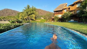 A swimming pool with clear blue water, surrounded by lush greenery and a mountain in the background. - Exclusive Manzanillo Bay Residencias 1-bdrm, seaside condo in charming Troncones (Troncones)