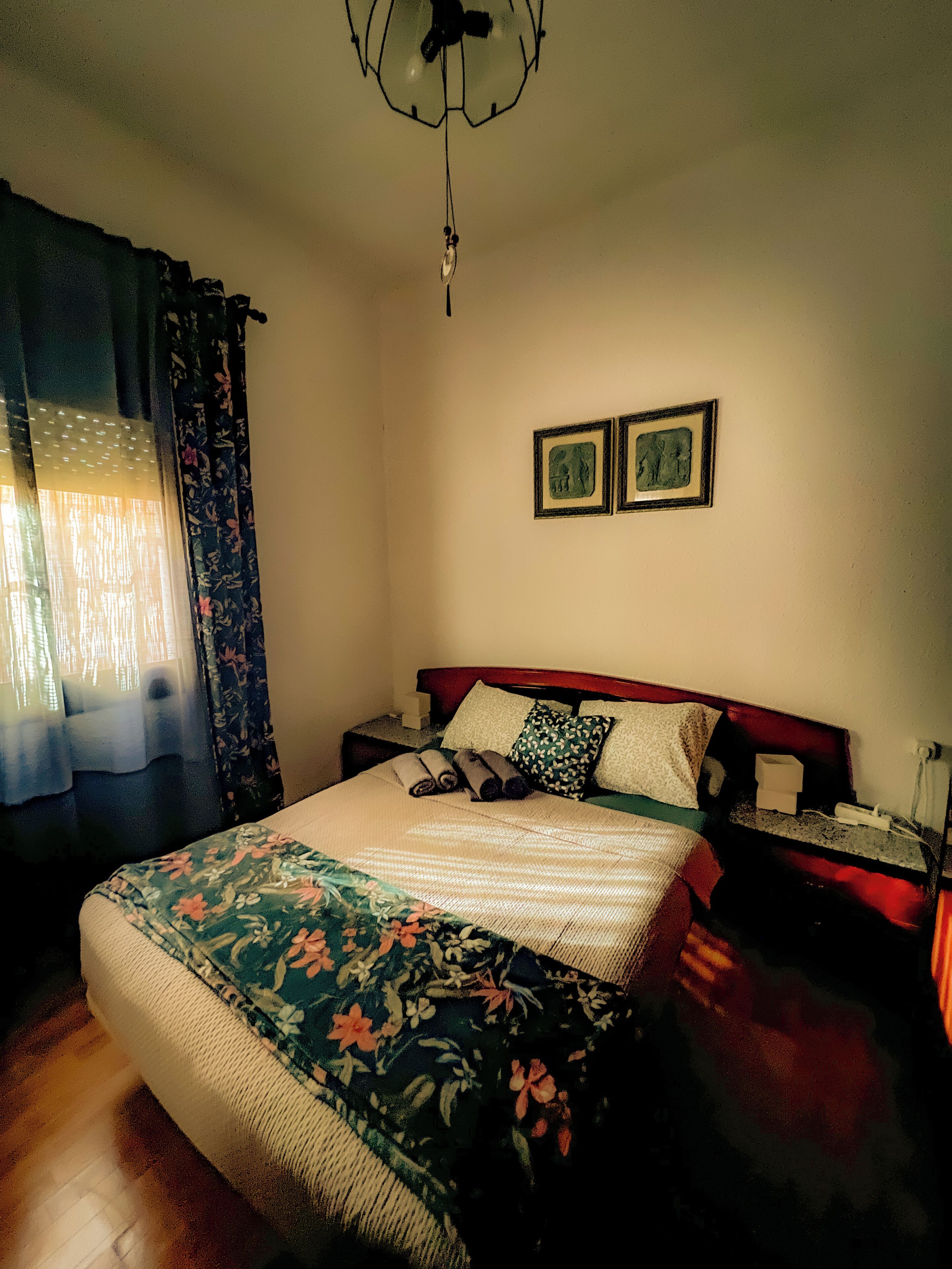 Une chambre à coucher avec un lit, des rideaux, une table de chevet et deux tableaux encadrés accrochés au mur.