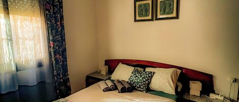 Une chambre à coucher avec un lit, des rideaux, une table de chevet et deux tableaux encadrés accrochés au mur.