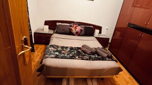 Un dormitorio con cama, armario de madera, mesitas de noche y una lámpara fijada a la pared.