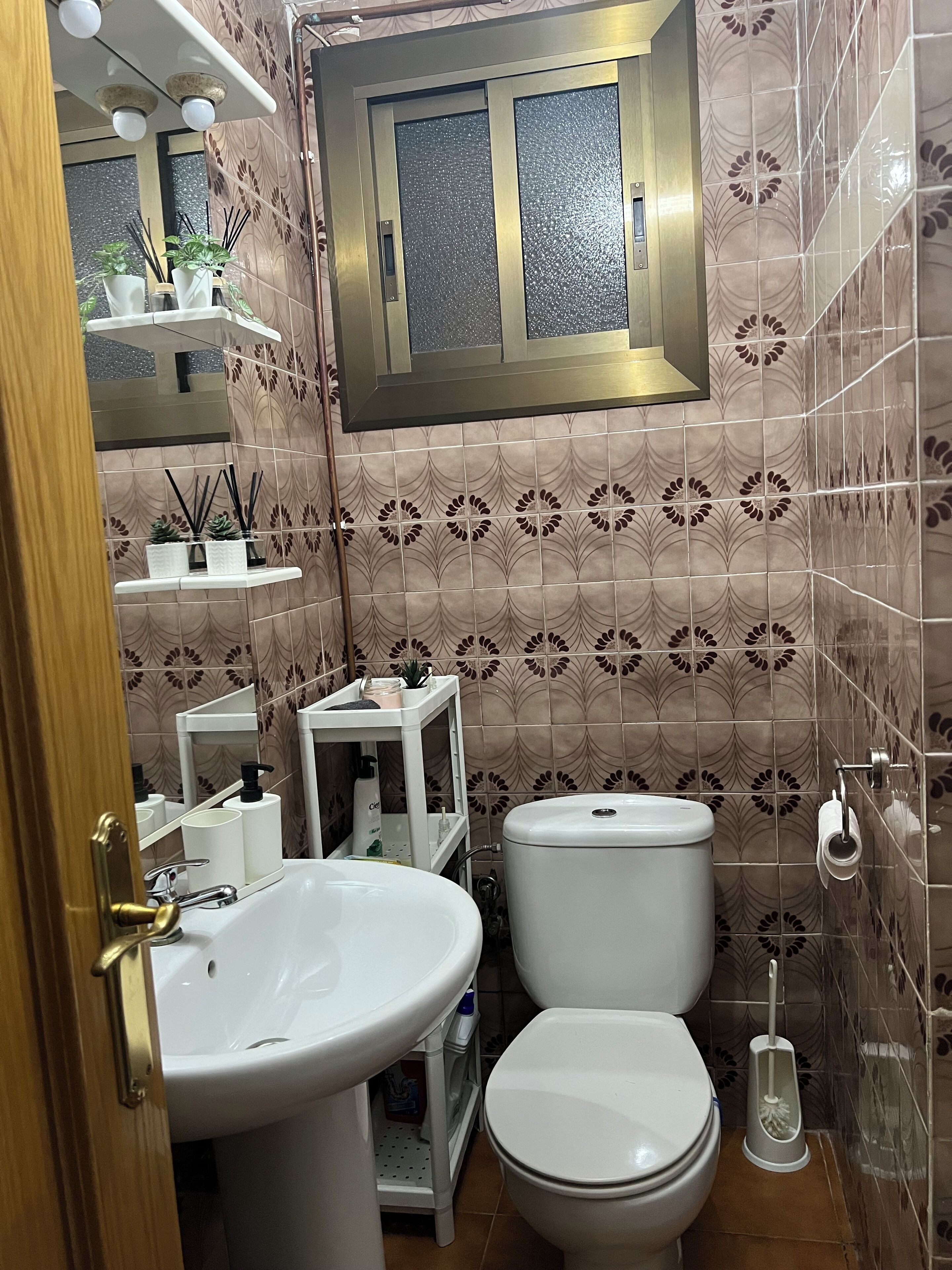 A bathroom with a toilet, sink, and a window above the mirror.