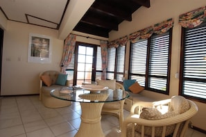 A spacious living room with a glass-top coffee table, wicker furniture, and large windows with blinds. - 5BR Villa, Pool & Little Bay Views (Little bay)
