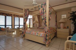A four-poster bed with floral curtains, a ceiling fan, and a view of the room's interior.