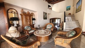 A spacious living area with wicker furniture, a round coffee table, and a staircase leading to an upper level. - 5BR Villa, Pool & Little Bay Views (Little bay)