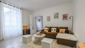 Een woonkamer met een zithoek, een salontafel en een bijzettafeltje. Er liggen twee kussens met 'HABIB' erop. Een deur leidt naar een andere kamer.