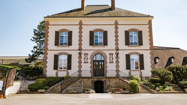 Een groot, historisch gebouw met een symmetrische gevel, meerdere ramen en een centrale ingang met een trap naar de hoofddeur.
