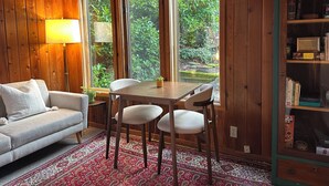 A cozy room with a wooden interior, a dining table with chairs, a sofa, a lamp, and a bookshelf.