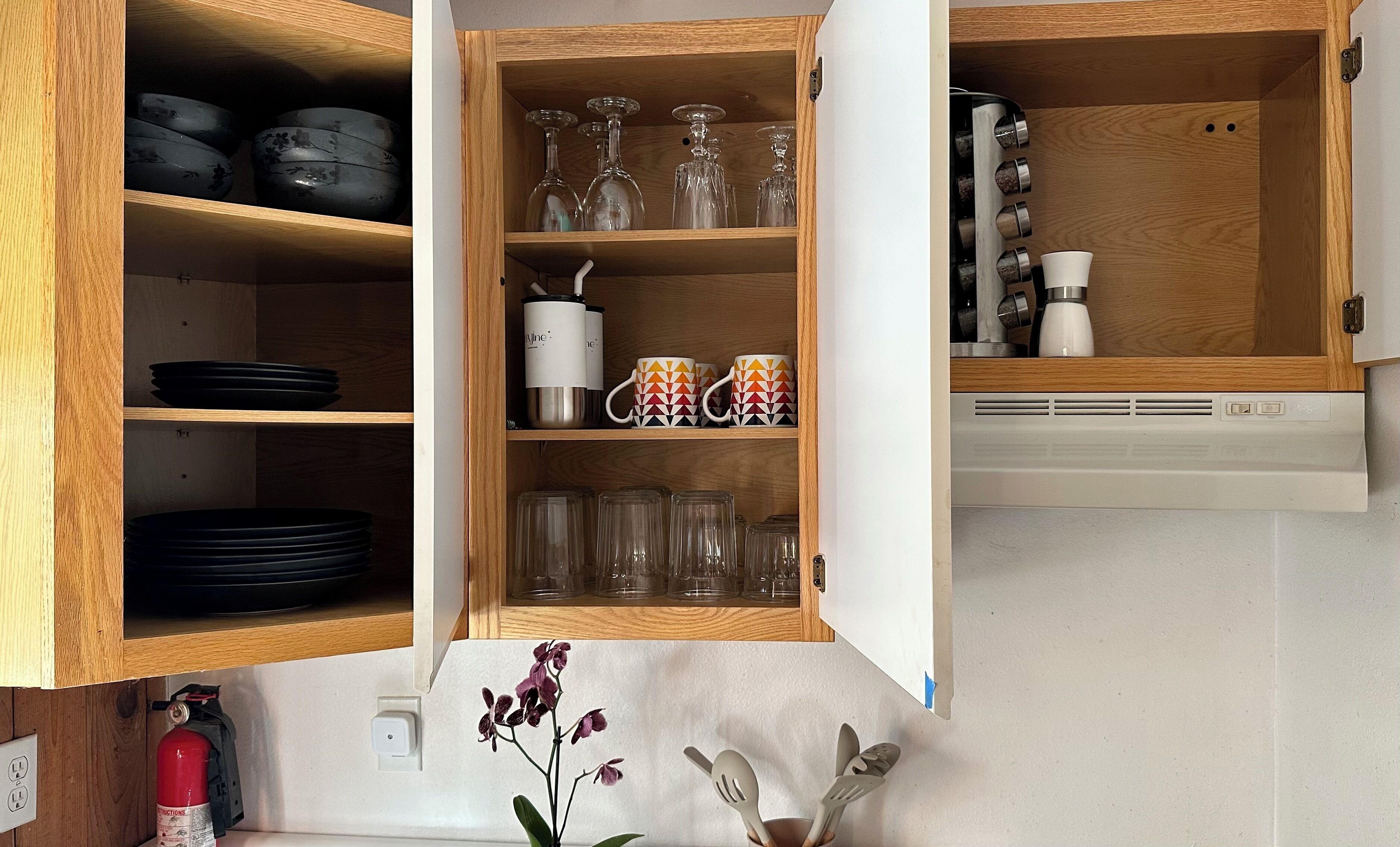 A kitchen with wooden cabinets, black plates, clear glassware, and a white appliance.