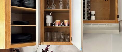 A kitchen with wooden cabinets, black plates, clear glassware, and a white appliance.