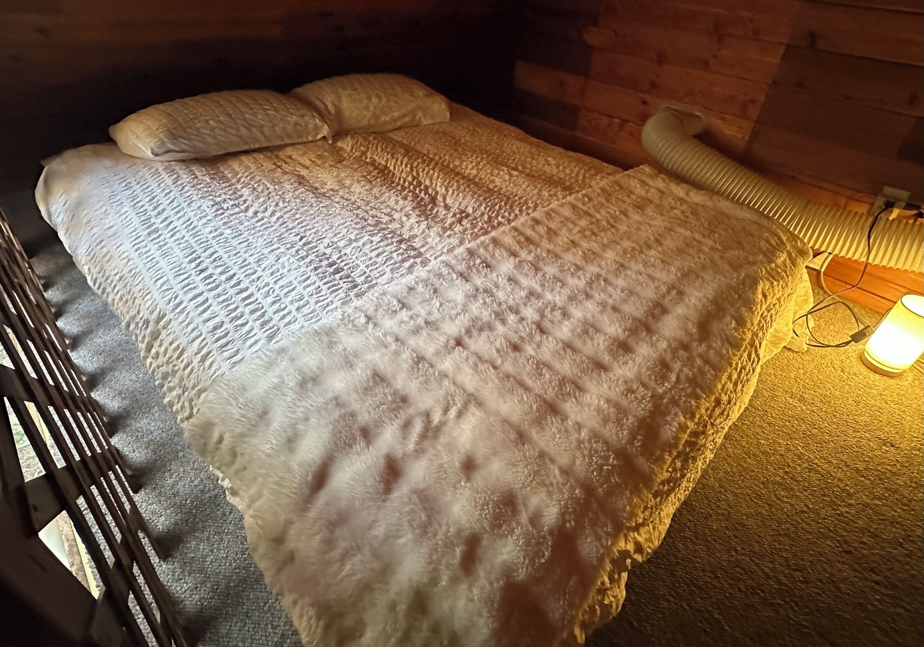 Un lit avec une couverture et des oreillers à motifs, une tête de lit en bois et une lampe sur la table de chevet.