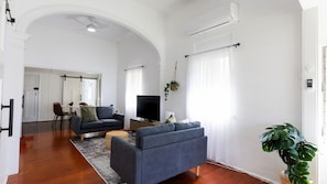 A living room with a sofa, TV, and a dining area with chairs and a table. - Charming Cottage Stay (South Townsville)