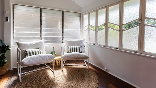 Une pièce avec deux chaises blanches, un tapis tissé et de grandes fenêtres aux carreaux de verre dépoli.