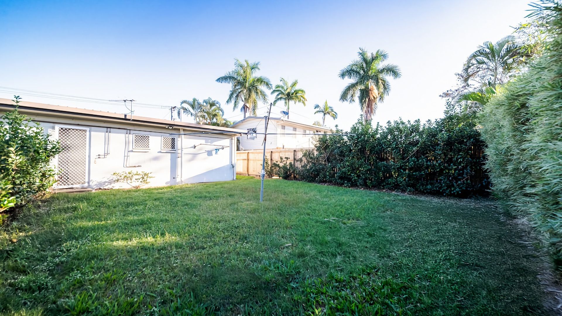 A residential property with a fenced yard, palm trees, and a white building with a garage.