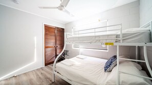 Quarto com beliche, ventilador de teto, porta de madeira e parede branca.