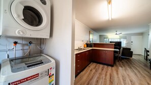 Cozinha compacta com máquina de lavar embutida, micro-ondas e área de refeições com sofá e mesa.