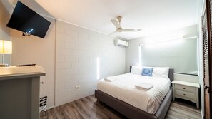 A hotel room with a bed, bedside table, TV, and a ceiling fan.