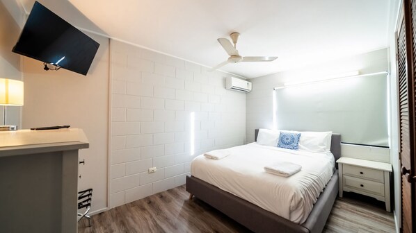 A hotel room with a bed, bedside table, TV, and a ceiling fan.