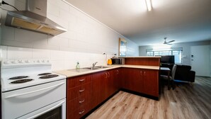 A modern kitchen with white cabinets, a stove, and a microwave. There's a dining area with a table and chairs, and a ceiling fan. - Comfy Kirwan Getaway (Kirwan)