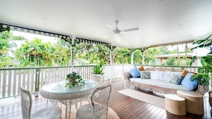 A covered outdoor area with a glass table and wicker chairs, a sofa with cushions, and a ceiling fan. - Tropical getaway 10 min to city Vacation Home in Hermit Park (Hermit Park)