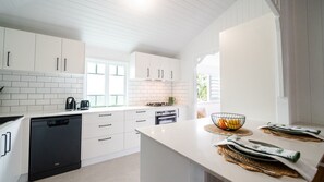 A modern kitchen with white cabinetry, a dishwasher, a stove, and a window providing natural light. - Tropical getaway 10 min to city Vacation Home in Hermit Park (Hermit Park)
