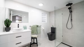 A modern bathroom with a white vanity, a round sink, a mirror, a potted plant, a glass shower enclosure, and a black trash bin. - Tropical getaway 10 min to city Vacation Home in Hermit Park (Hermit Park)