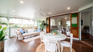 A covered outdoor area with a wooden deck, a white wicker dining set, and a cushioned seating area with a ceiling fan. - Tropical getaway 10 min to city Vacation Home in Hermit Park (Hermit Park)