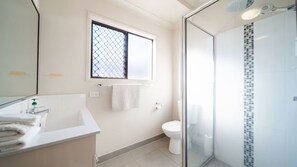 Een moderne badkamer met een douchecabine van glas, een witte wastafel en een toilet.