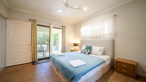 Een slaapkamer met een bed, nachtkastje, plafondventilator en uitzicht door een deur.