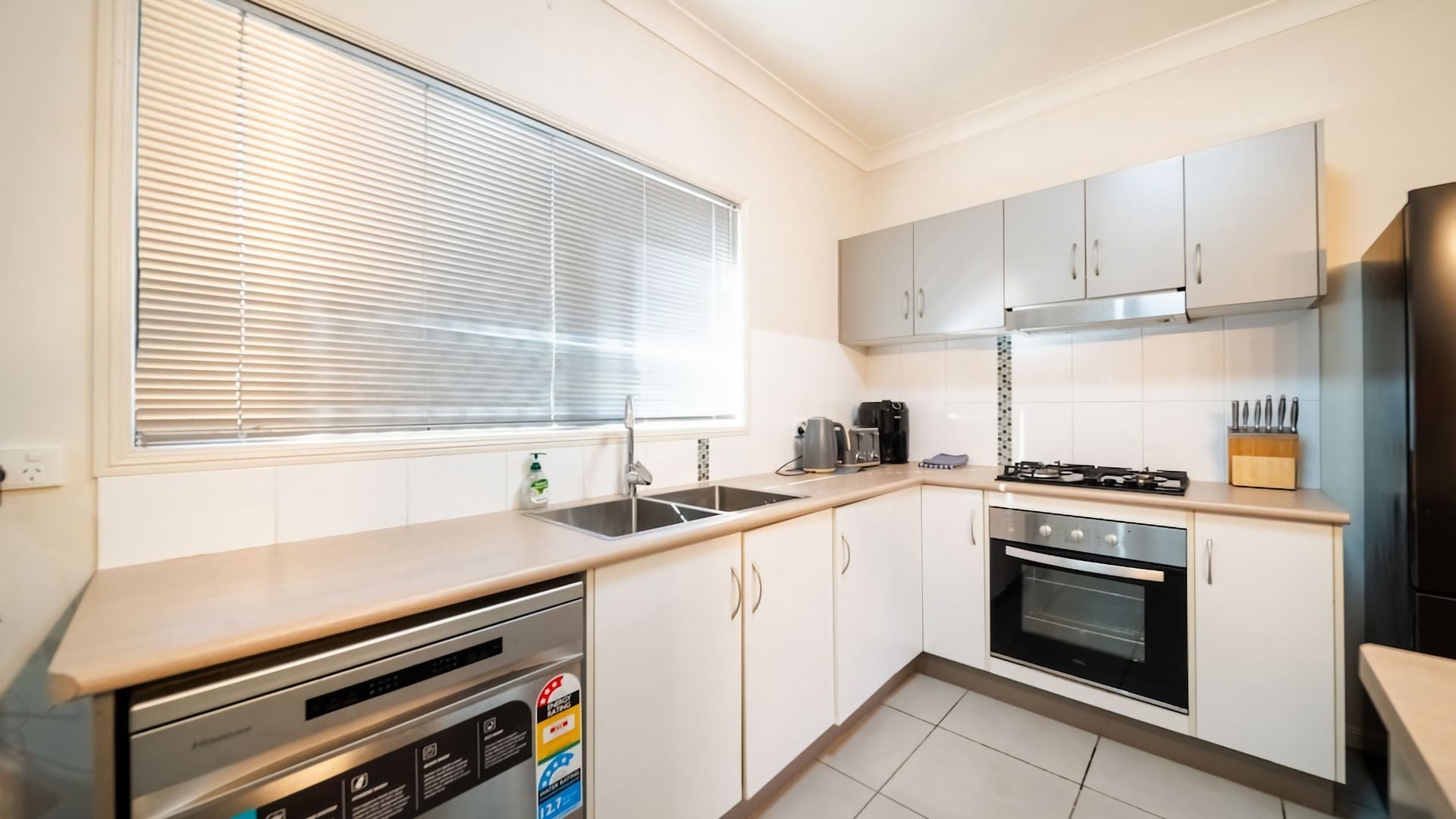A modern kitchen with a dishwasher, stove, oven, and a window with blinds.